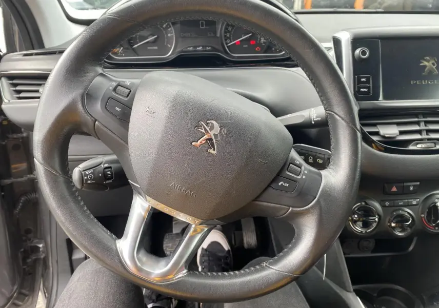 Vue rapprochée du volant cuir noir et du tableau de bord d'une Peugeot 208 gris métallisé de 2018 avec commandes intégrées.