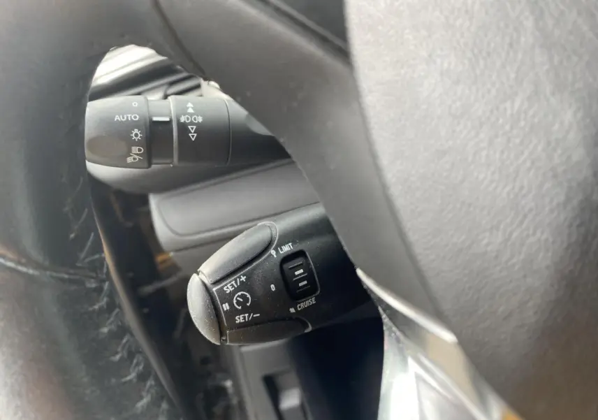 Gros plan sur la commande de régulateur de vitesse et allumage automatique des feux dans un Peugeot 208 gris, vue côté conducteur.
