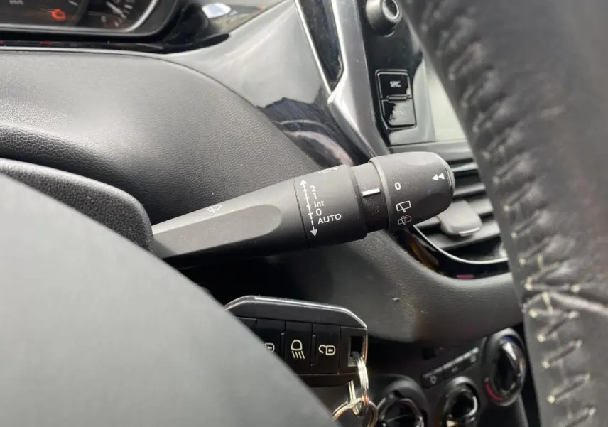 Gros plan sur la commande d’essuie-glace côté gauche du tableau de bord noir d’une Peugeot 208 gris métallisé.