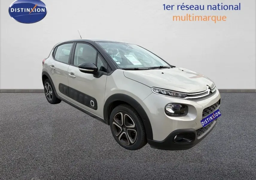 Citroën C3 beige vue 3/4 avant droit, avec protections latérales noires et jantes spécifiques, stationnée devant un mur blanc.