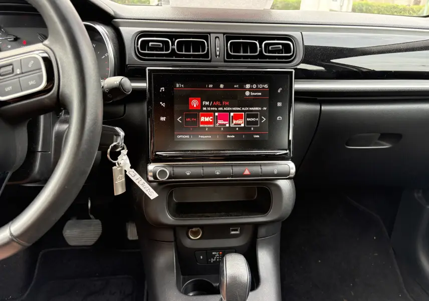 Vue intérieure centrée sur la console centrale noire de la Citroën C3 beige, avec écran tactile et volant partiel visible.