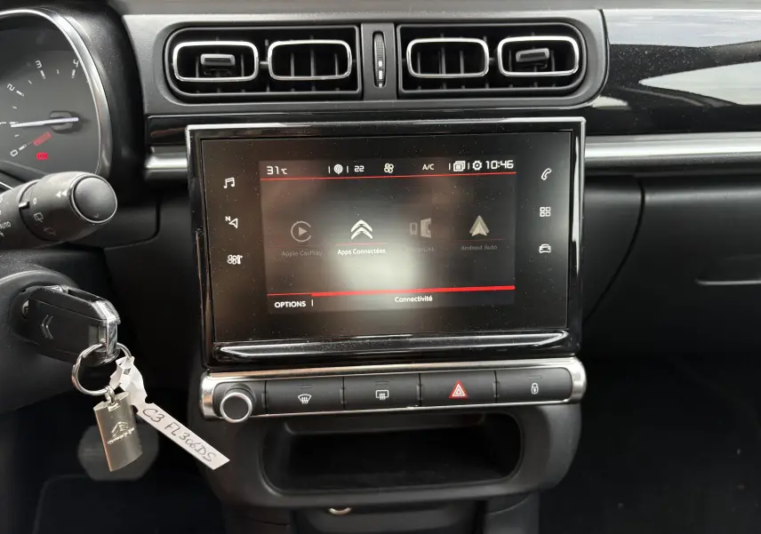 Vue rapprochée de l’écran tactile central et tableau de bord noir du Citroën C3 beige, avec commandes climatisation et clé insérée.