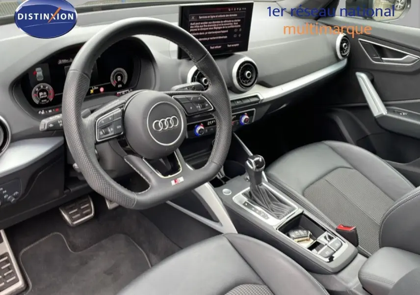 Vue intérieure côté conducteur de l'Audi Q2 35 2.0 TDI S-Line 2025 avec volant cuir perforé et console centrale moderne.