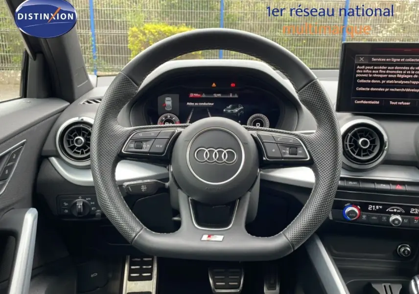 Vue intérieure centrée sur le volant sport perforé de l'Audi Q2 S-Line 2025 avec tableau de bord numérique et écran central.