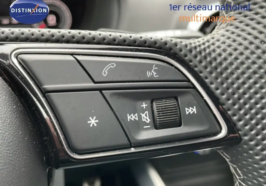 Gros plan sur les commandes noires au volant perforé de l’Audi Q2 noir mito metal, version 35 2.0 TDI S-Line.