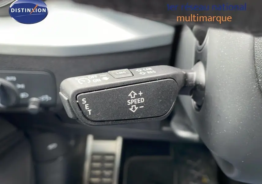 Gros plan sur la commande de régulateur de vitesse au volant d’un Audi Q2 noir mito metal, intérieur visible en arrière-plan.