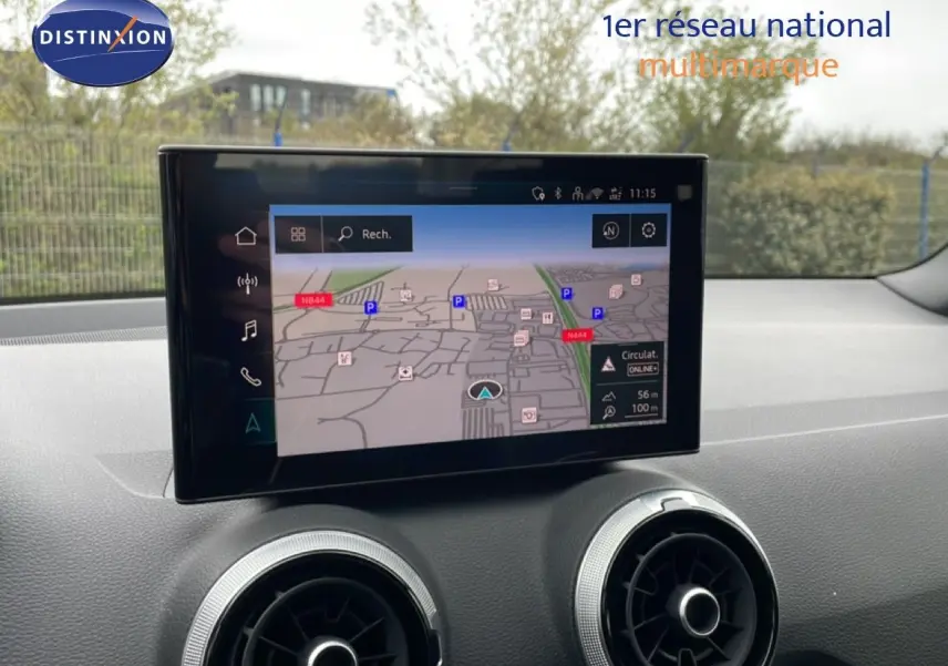 Vue intérieure du tableau de bord de l'Audi Q2 2025 avec écran tactile affichant la navigation et aérateurs ronds argentés.
