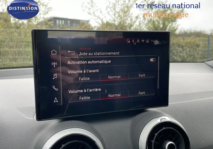 Écran central tactile de l’Audi Q2 2025 affichant les réglages d’aide au stationnement et volume sonore, intérieur noir.