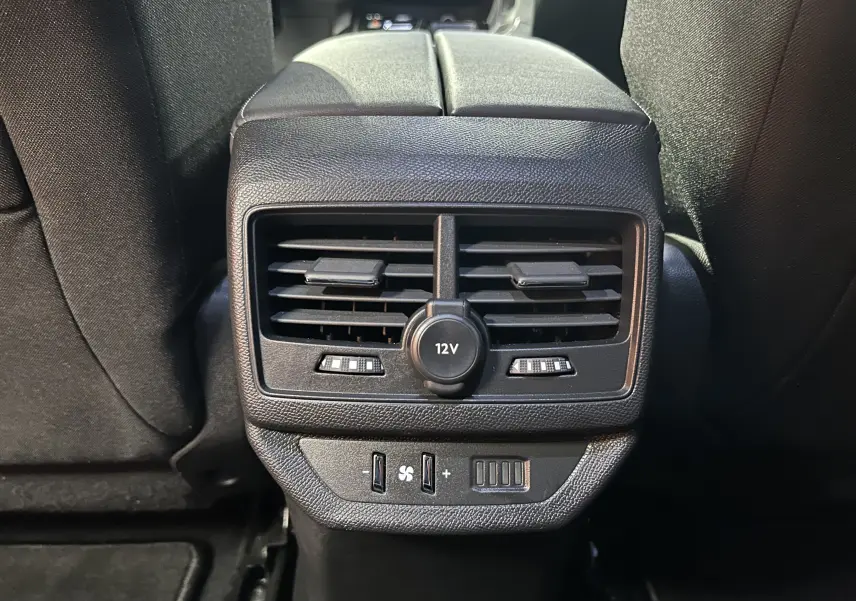 Vue rapprochée des aérateurs arrière et prise 12V noirs du Peugeot 5008 2024, entre les sièges arrière.