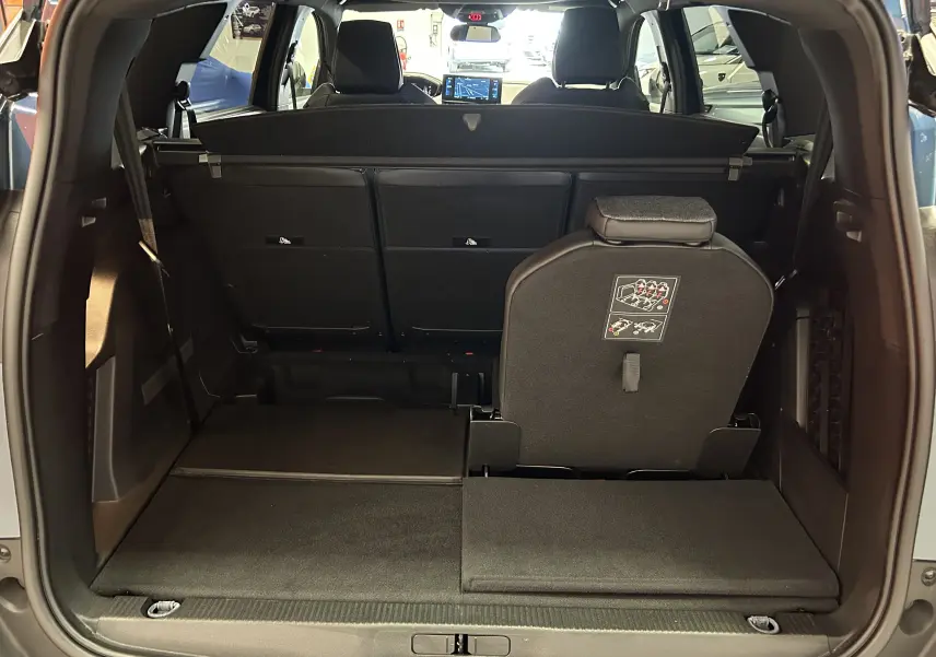 Coffre ouvert vu de l'arrière d'un Peugeot 5008 Bleu Célèbes 2024, siège arrière droit partiellement relevé.
