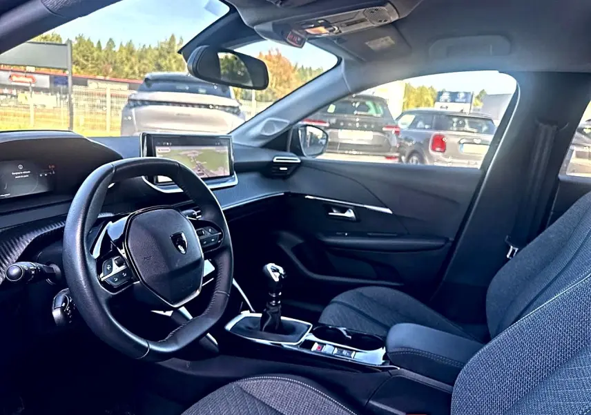 Intérieur de la Peugeot 208 1.2 100 allure noir, vue côté conducteur, volant compact et écran tactile central visible.