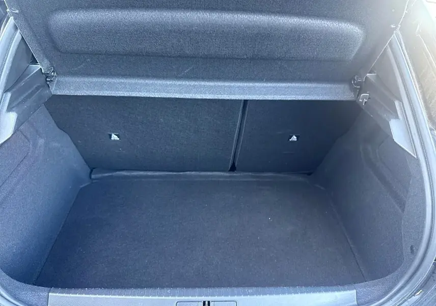 Coffre ouvert vu de face d’une Peugeot 208 noire, montrant l’espace de chargement vide et la tablette cache-bagages relevée.