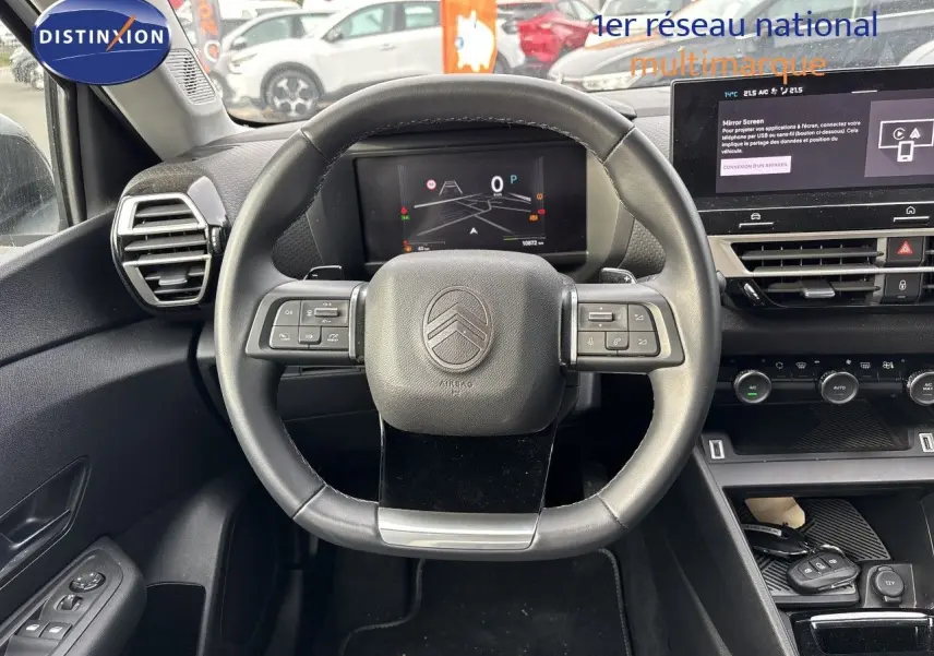 Vue intérieure centrée sur le volant cuir noir d’une Citroën C4 hybride 2025 avec tableau de bord digital et écran tactile.