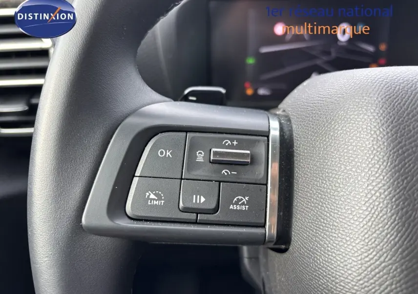 Gros plan sur les commandes au volant côté gauche d’un Citroën C4 blanc Okenite Metal, avec boutons de régulateur et assistance.