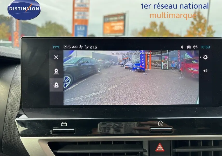 Écran central affichant la caméra de recul d'une Citroën C4 blanche, vue arrière du parking multimarque.
