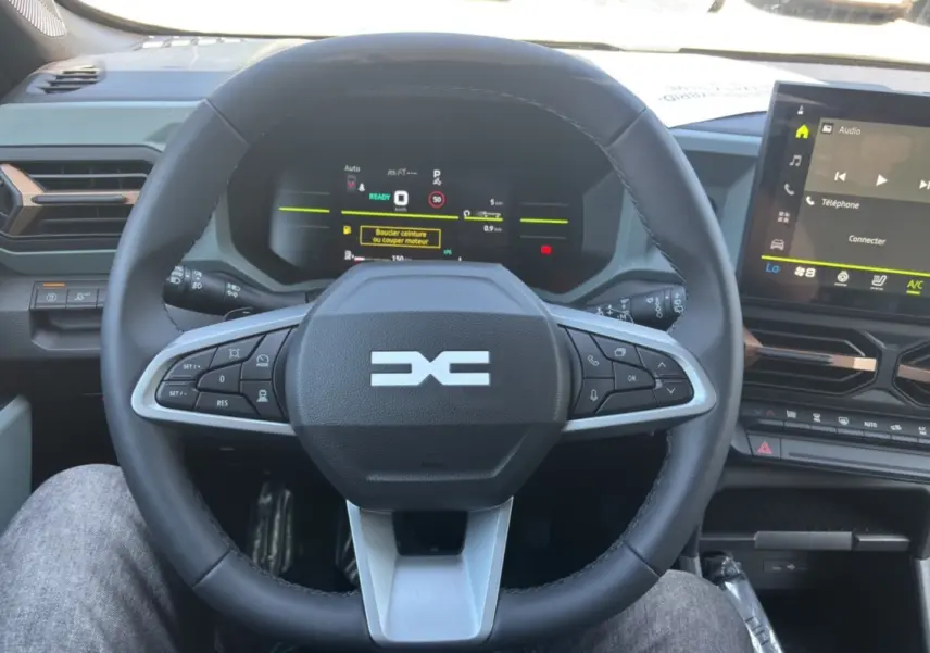 Vue centrée sur le volant cuir du Dacia Duster Hybrid-G 150 4x4, avec tableau de bord numérique et écran tactile visible.