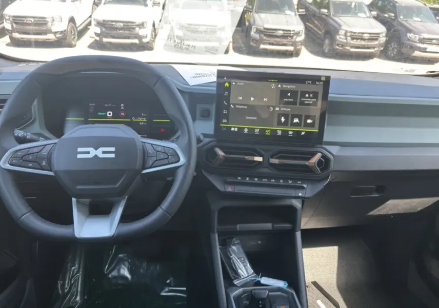 Vue intérieure du tableau de bord du Dacia Duster Hybrid-G 150, avec écran tactile et volant cuir noir.