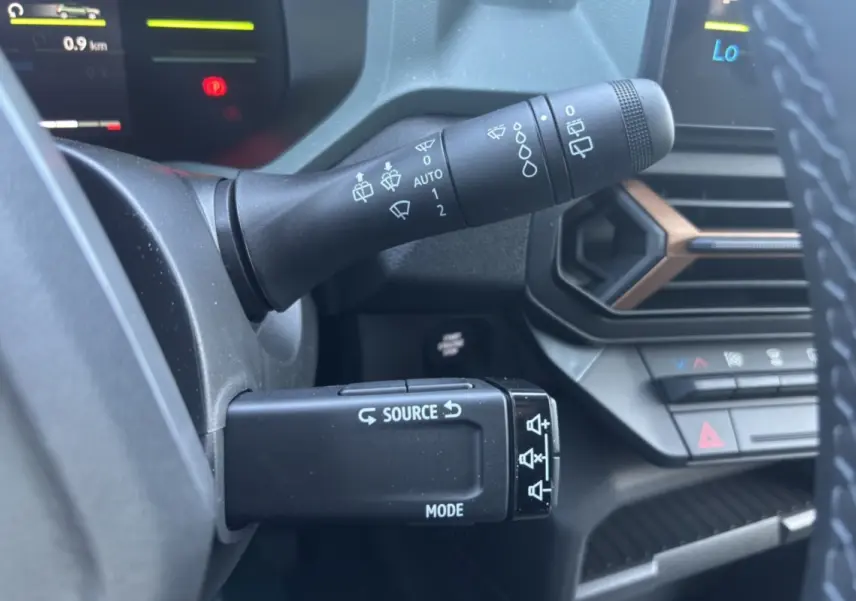 Gros plan sur les commandes au volant du Dacia Duster Hybrid-G 150 4x4, avec tableau de bord et aérateurs noirs et bronze.
