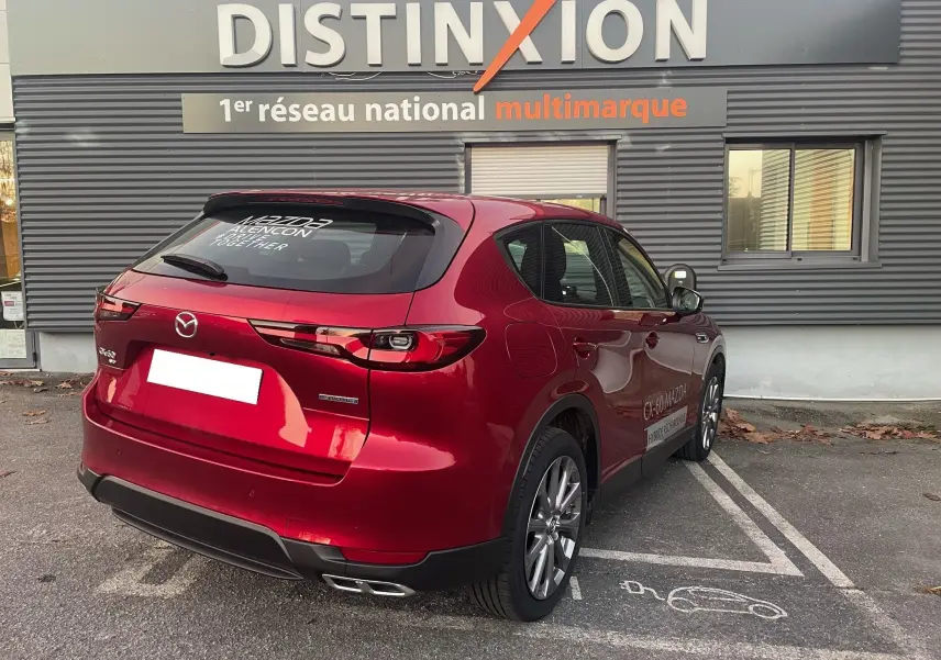 Vue 3/4 arrière droite d'un Mazda CX-60 hybride rechargeable Soul Red Crystal garé devant un bâtiment Distinxion.