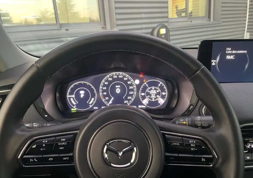 Vue depuis le siège conducteur sur le volant noir Mazda CX-60 et le tableau de bord numérique allumé.