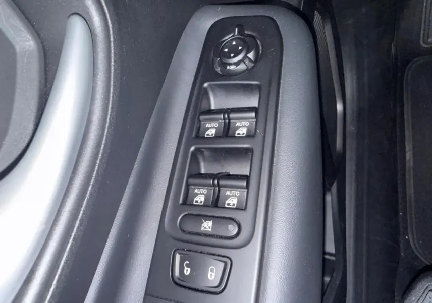 Gros plan sur les commandes des vitres électriques et rétroviseurs côté conducteur du Jeep Renegade gris anthracite 2024.