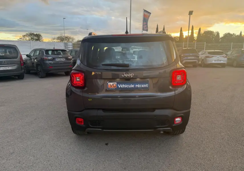 Vue arrière d'un Jeep Renegade gris anthracite 2024 avec feux arrière allumés sur un parking au coucher du soleil.