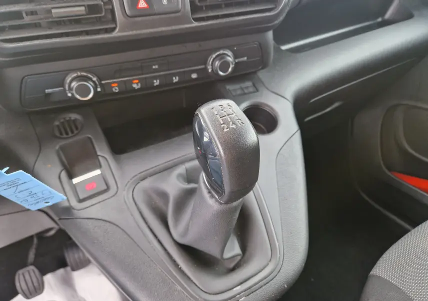 Gros plan sur le levier de vitesses manuel noir du Citroën Berlingo blanc, avec la console centrale et commandes de climatisation visibles.
