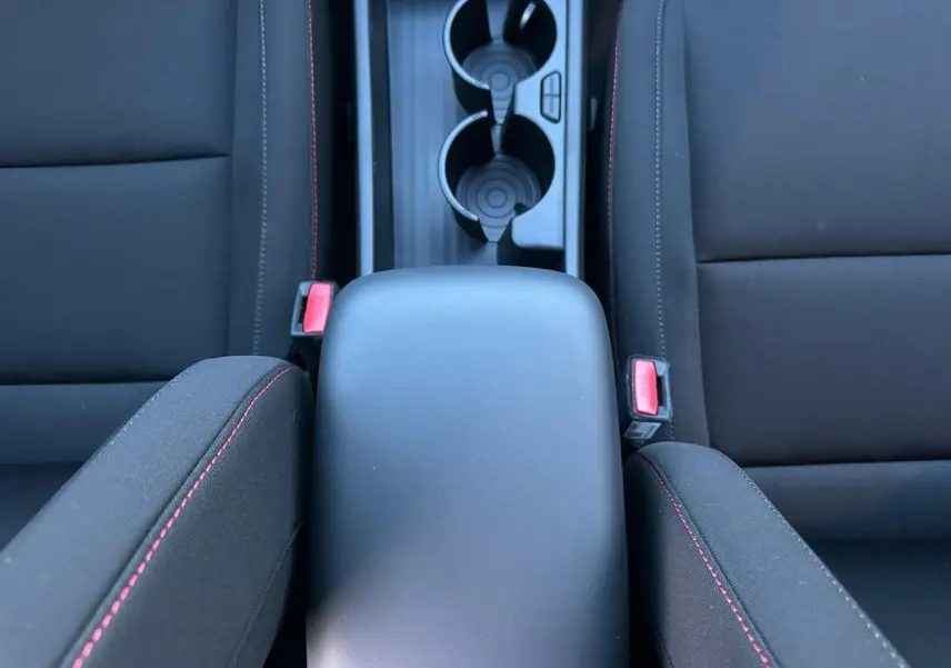 Vue plongeante sur l'accoudoir central noir et les sièges avant noirs avec surpiqûres rouges du Hyundai Kona 2026.