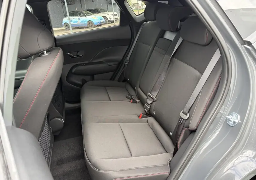 Vue intérieure côté droit sur la banquette arrière noire avec surpiqûres rouges du Hyundai KONA II Ecotronic Grey.