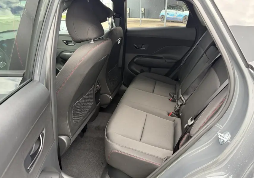 Vue côté droit de l’habitacle arrière du Hyundai KONA 2026 gris Ecotronic, sièges tissu avec surpiqûres rouges.