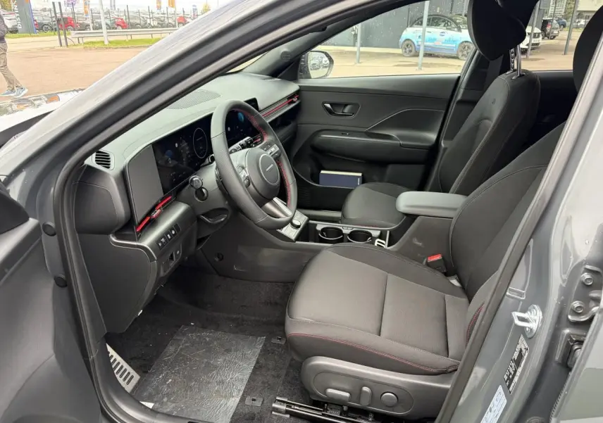 Vue intérieure côté conducteur du Hyundai Kona gris Ecotronic, avec tableau de bord numérique et volant cuir à surpiqûres rouges.