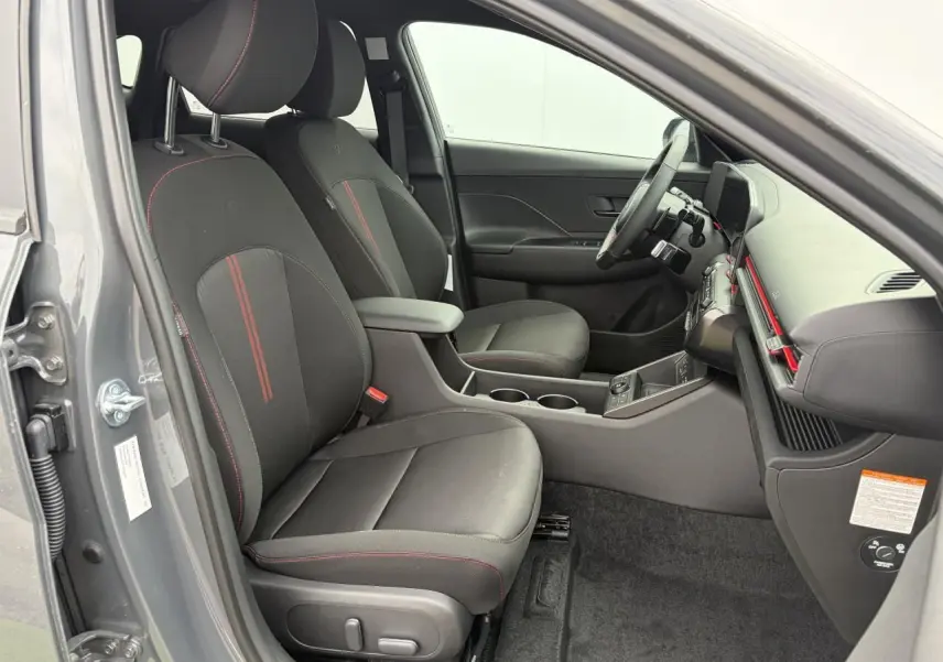 Vue intérieure côté conducteur du Hyundai Kona II 2026 gris Ecotronic, sièges noirs avec surpiqûres rouges et console centrale.