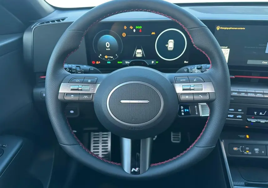 Vue rapprochée du volant cuir noir avec surpiqûres rouges du Hyundai Kona 2026, tableau de bord numérique et commandes intégrées.