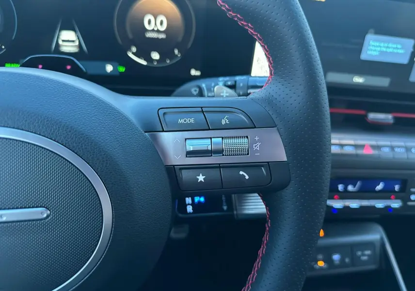 Vue rapprochée du volant cuir perforé avec surpiqûres rouges et commandes multifonctions du Hyundai Kona 2026.