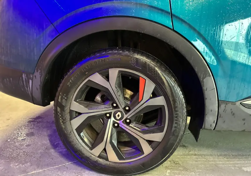 Gros plan sur la roue arrière droite du Renault Arkana bleu 1.3 TCE 140 RS-LINE avec jante alliage noire et détail rouge.