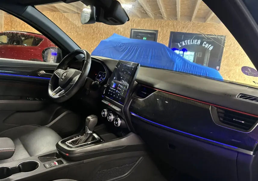 Intérieur noir du Renault Arkana 1.3 TCE 140 RS-LINE vu côté conducteur, avec écran tactile vertical et éclairage d'ambiance bleu.