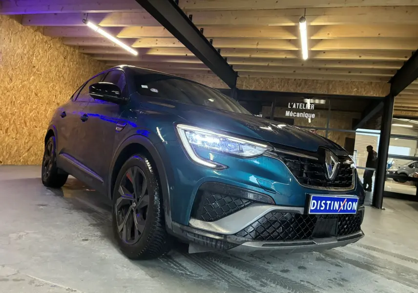 Vue 3/4 avant gauche d’un Renault Arkana bleu 2021 RS-Line avec calandre noire et phares LED allumés dans un garage.