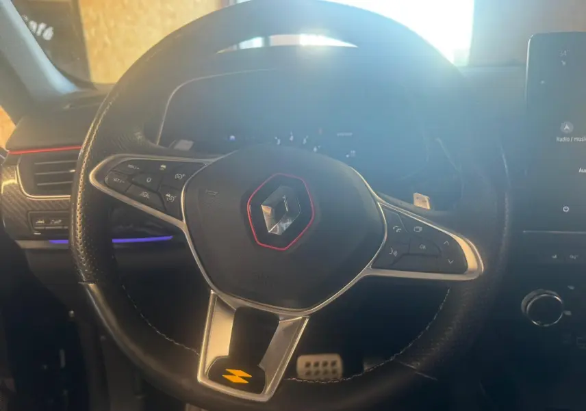 Gros plan sur le volant noir perforé du Renault Arkana 1.3 TCE 140 RS-LINE avec logo rouge et commandes intégrées.