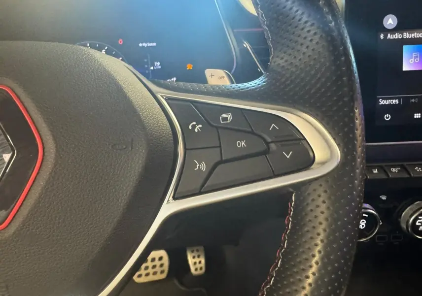 Gros plan sur le volant en cuir noir perforé du Renault Arkana 1.3 TCE 140 RS-LINE avec commandes intégrées et surpiqûres rouges.