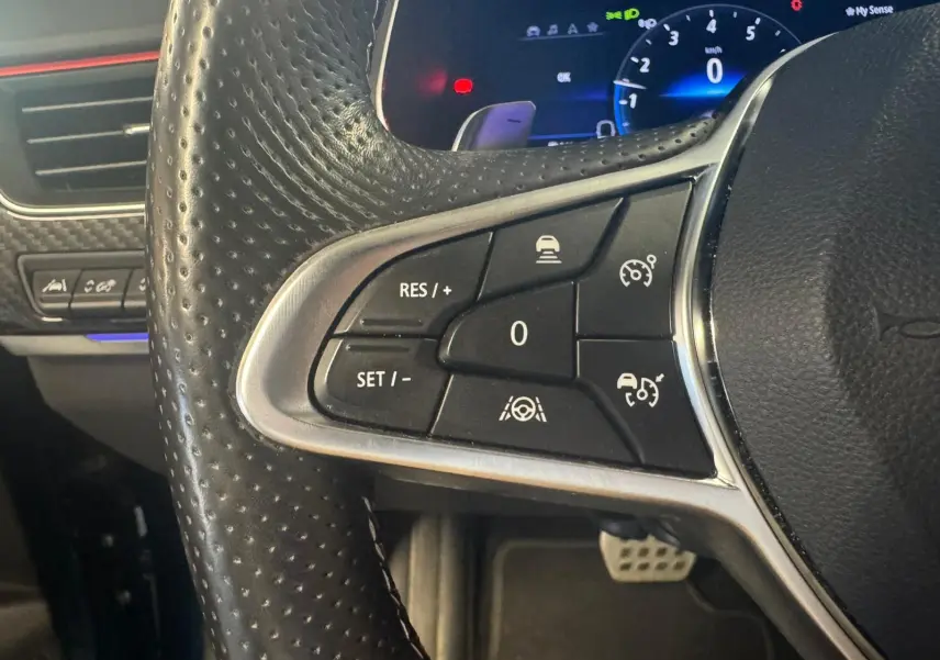 Gros plan sur les commandes au volant côté gauche du Renault Arkana bleu 1.3 TCE 140 RS-LINE avec affichage numérique en arrière-plan.