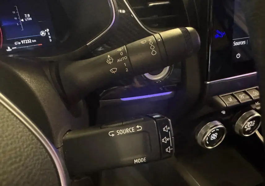 Gros plan sur les commandes de volant et tableau de bord noir du Renault Arkana bleu, avec affichage digital et régulateur de climatisation.