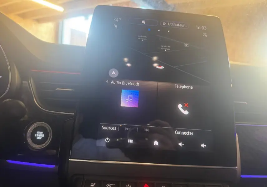 Écran tactile central allumé avec navigation et commandes multimédia dans l'habitacle noir du Renault Arkana bleu.