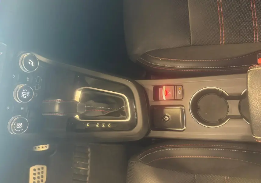 Vue plongeante sur la console centrale noire du Renault Arkana bleu, avec levier de vitesse automatique et sièges à surpiqûres rouges.