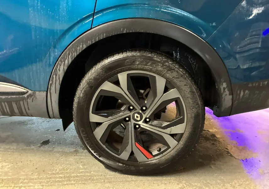 Gros plan sur la roue arrière droite du Renault Arkana bleu 1.3 TCE 140 RS-LINE avec jante noire et détail rouge.