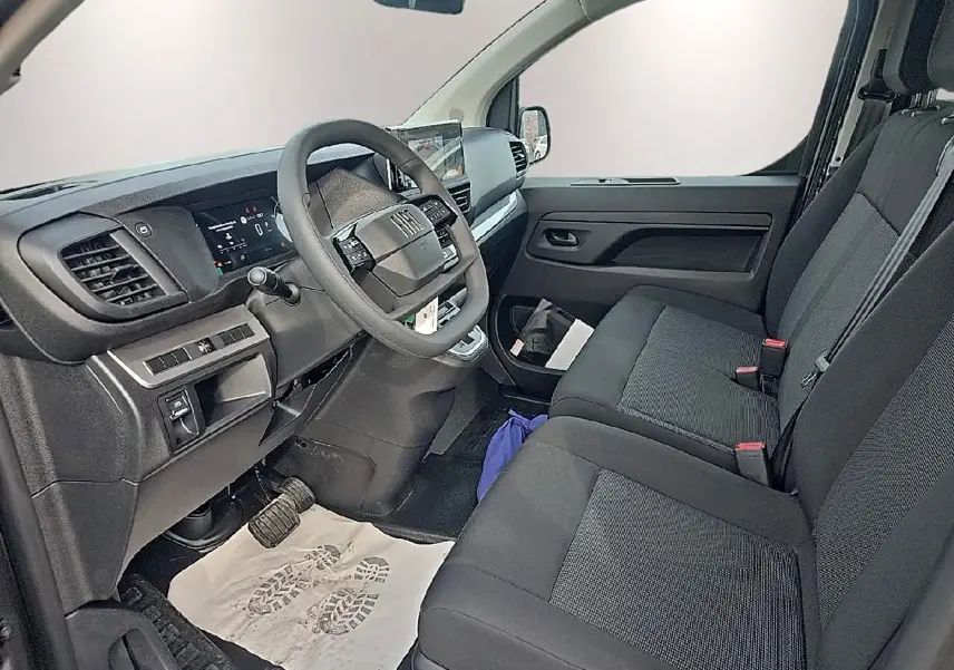 Vue intérieure côté conducteur du Fiat Scudo Combi 2026, sièges tissu bi-ton noir/gris et tableau de bord moderne.