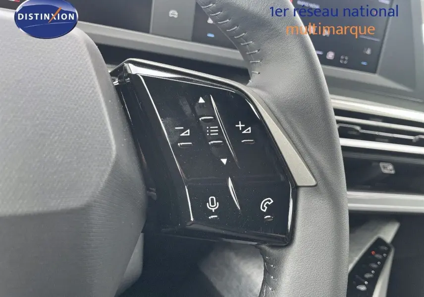 Gros plan sur les commandes gauche du volant noir cuir du Peugeot 3008 Hybrid 2025, avec tableau de bord numérique en arrière-plan.