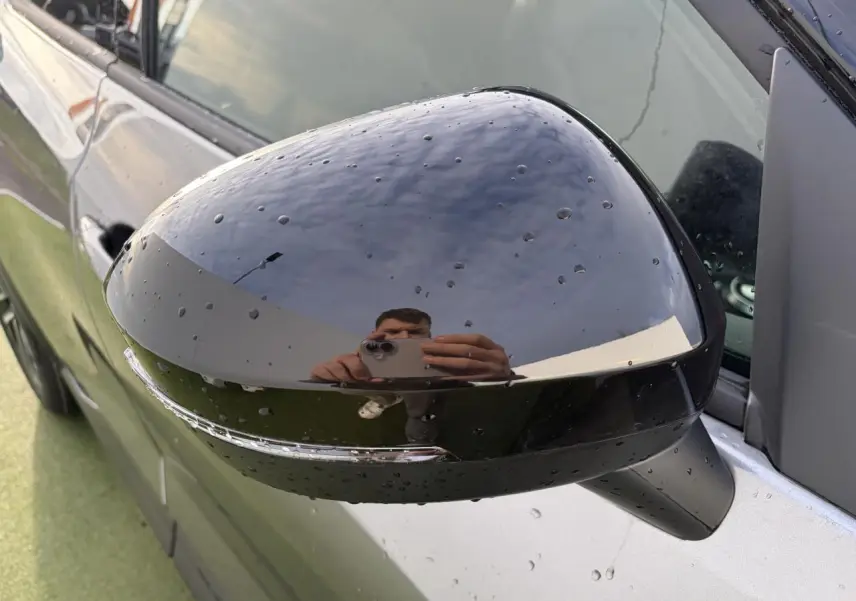 Rétroviseur noir métallisé côté gauche du Nissan Juke II 1.6 Hybrid 143 N-Connecta avec gouttes d'eau visibles.