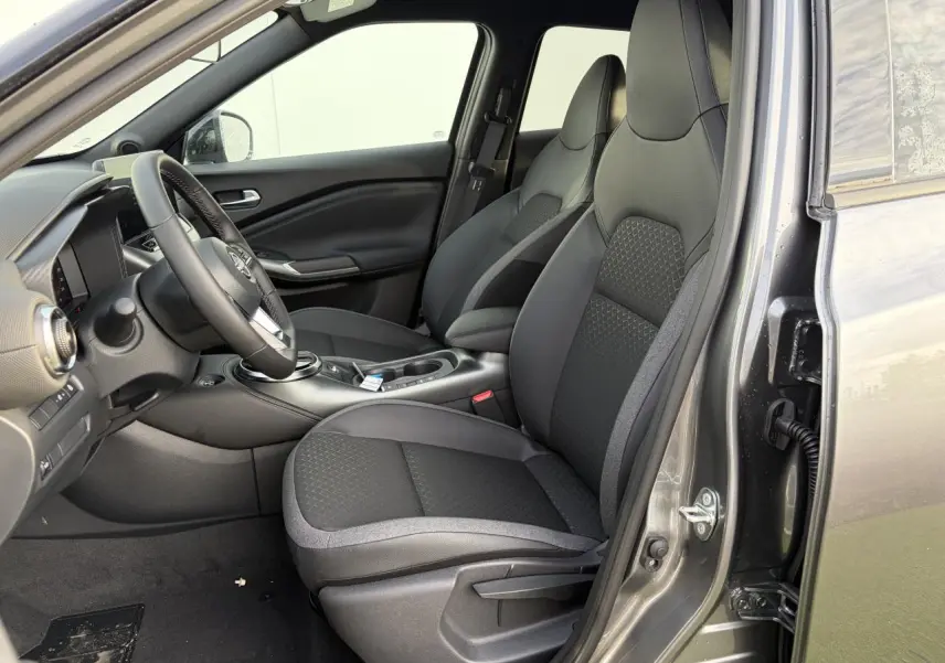 Vue intérieure côté conducteur du Nissan Juke II 1.6 Hybrid 2025, sièges en tissu noir et gris avec console centrale visible.