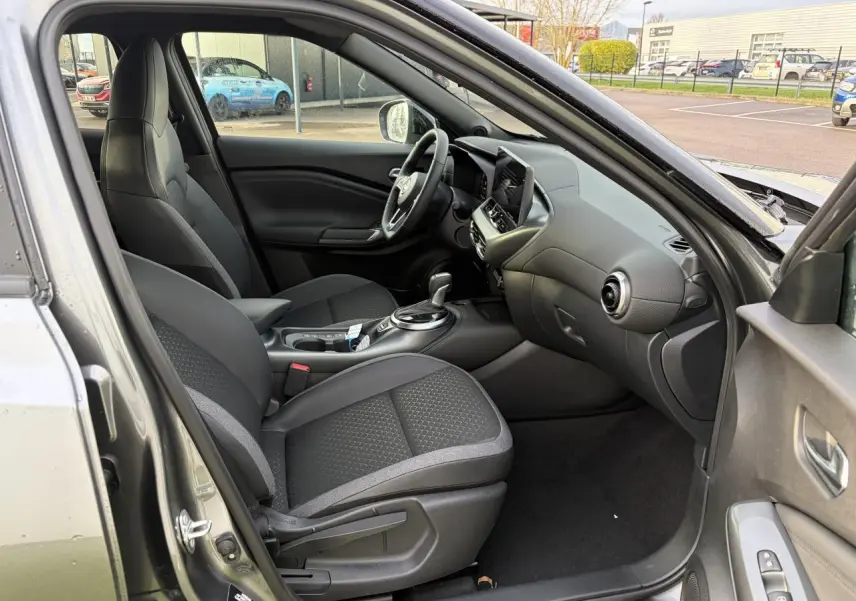 Vue intérieure côté conducteur du Nissan Juke II noir métal, montrant les sièges, volant cuir et console centrale moderne.
