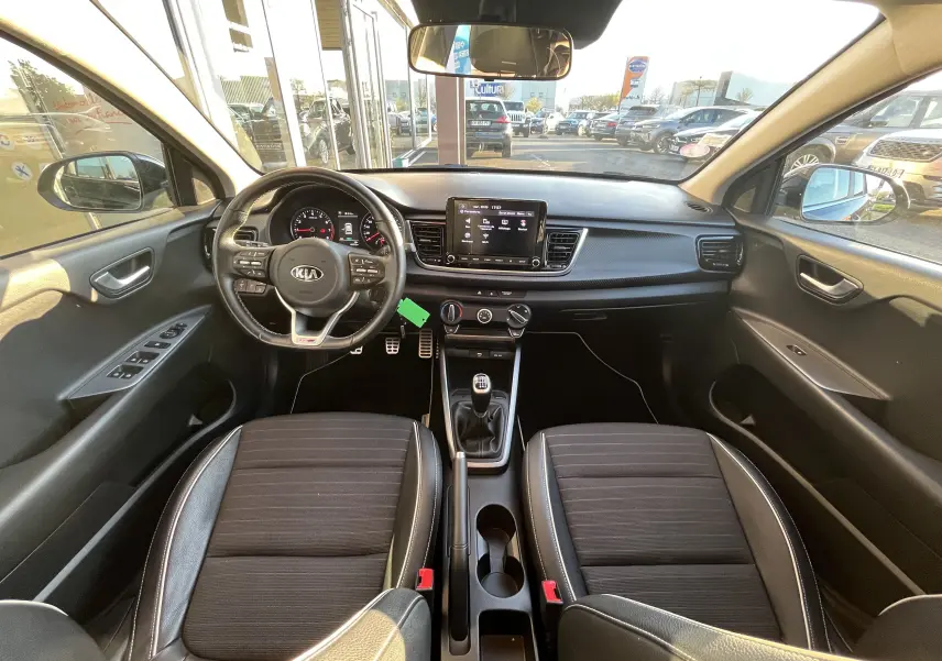 Vue intérieure avant de la KIA RIO noire 2021, montrant le volant multifonction, la console centrale et les sièges tissu avec surpiqûres.